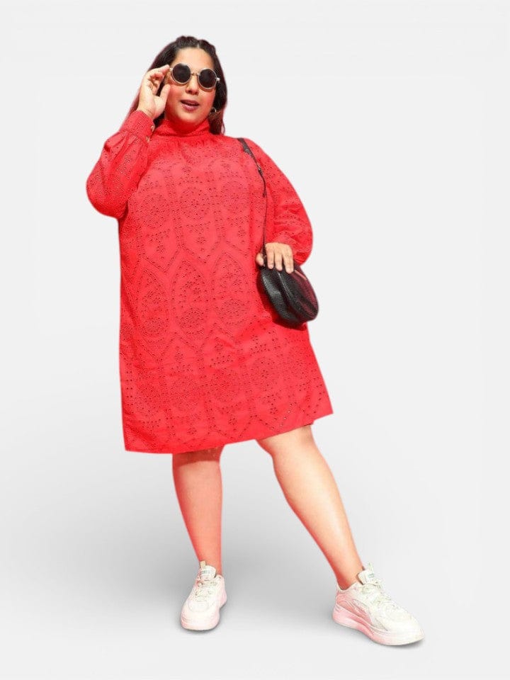 A woman wearing a red dress and sunglasses, holding a black purse, and wearing white sneakers.
