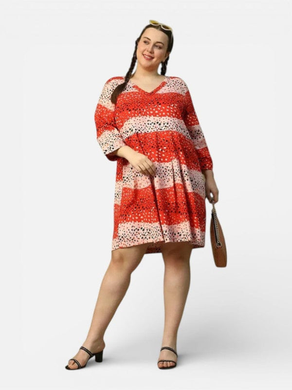 A woman wearing a red and white polka dot dress and sunglasses, smiling and holding a brown purse, standing against a white background.