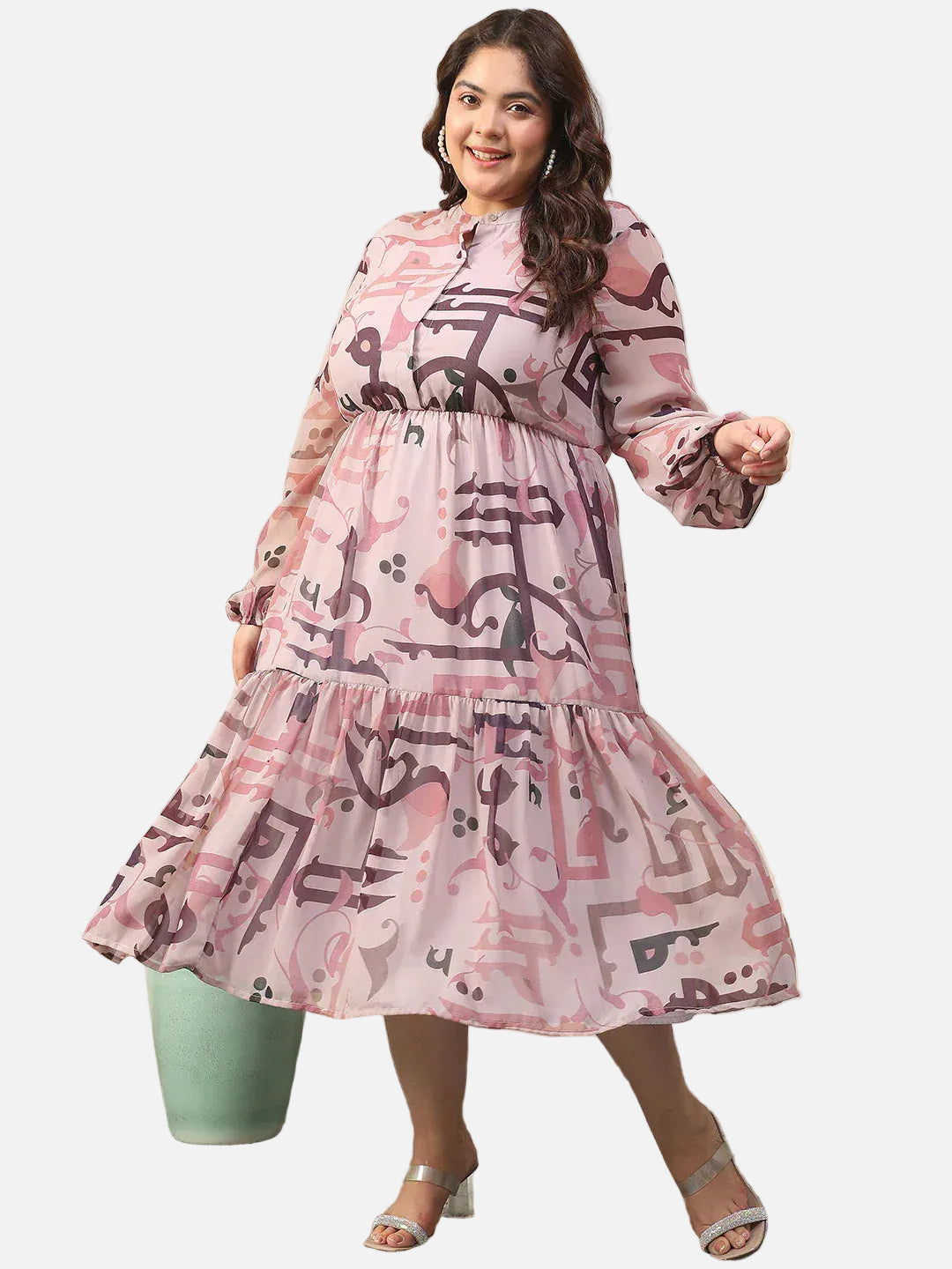 A woman wearing a pink and purple patterned dress with a high neckline and long sleeves, smiling and posing with her hand in her pocket.