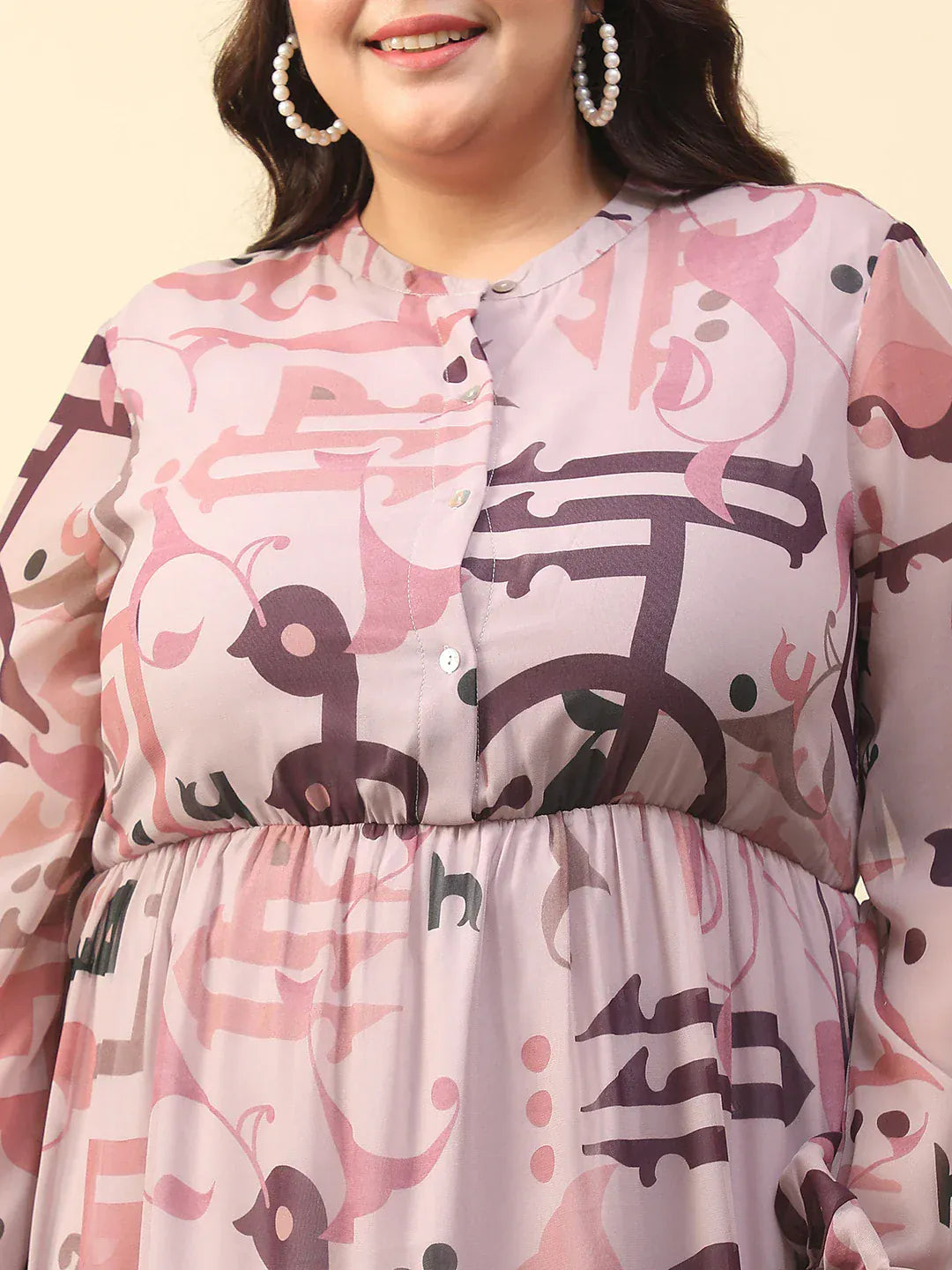 A woman wearing a pink and purple patterned dress with a high neckline and long sleeves, smiling and posing with her hand in her pocket.