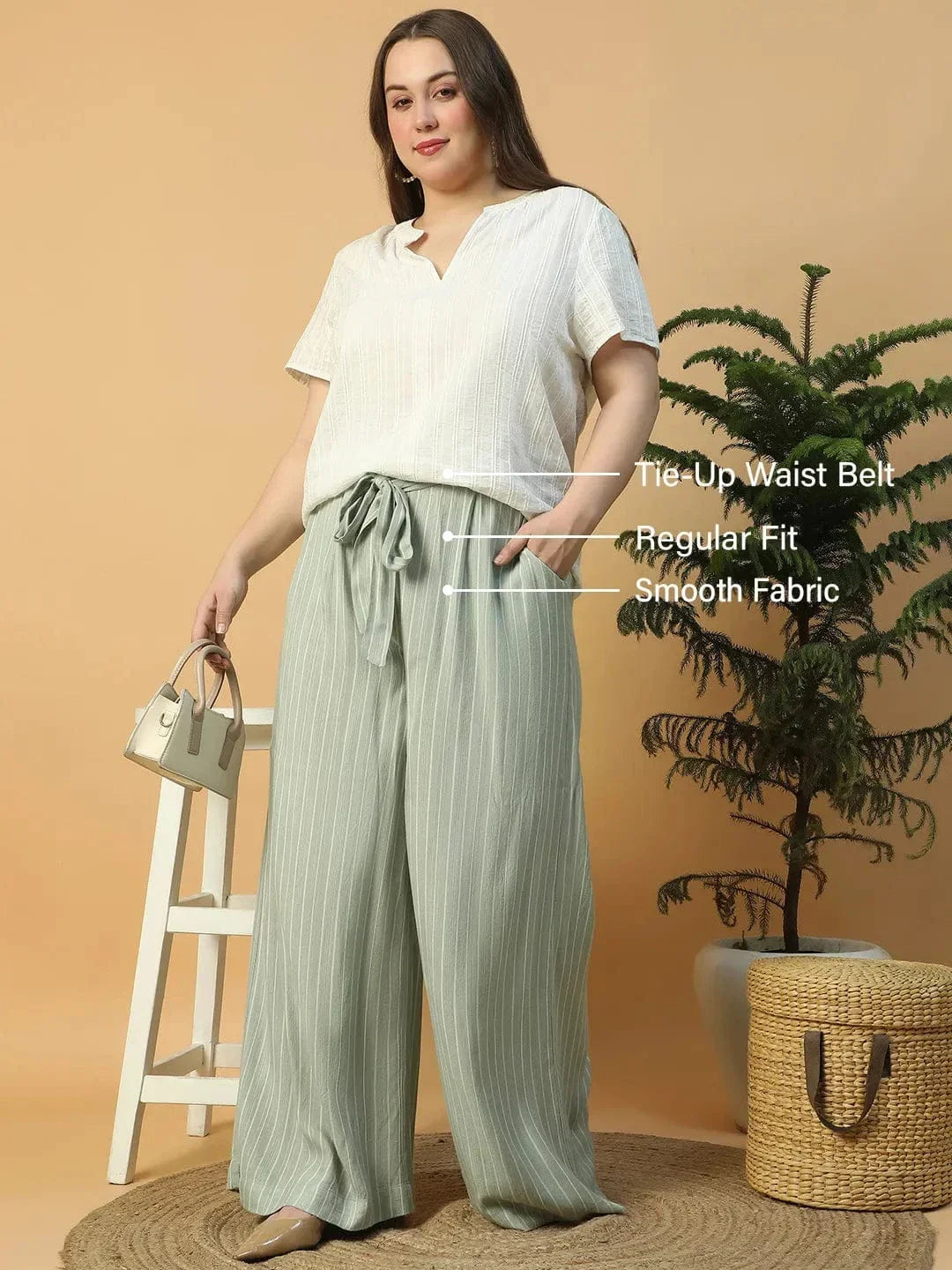 A woman wearing a white top and green striped pants is posing with her hand on her head.