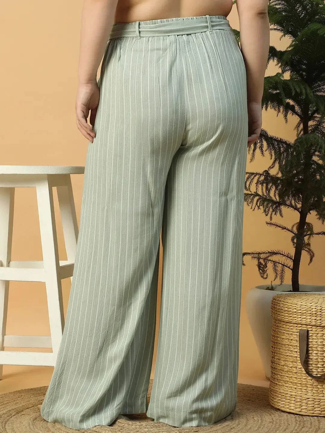 A woman wearing a white top and green striped pants is posing with her hand on her head.