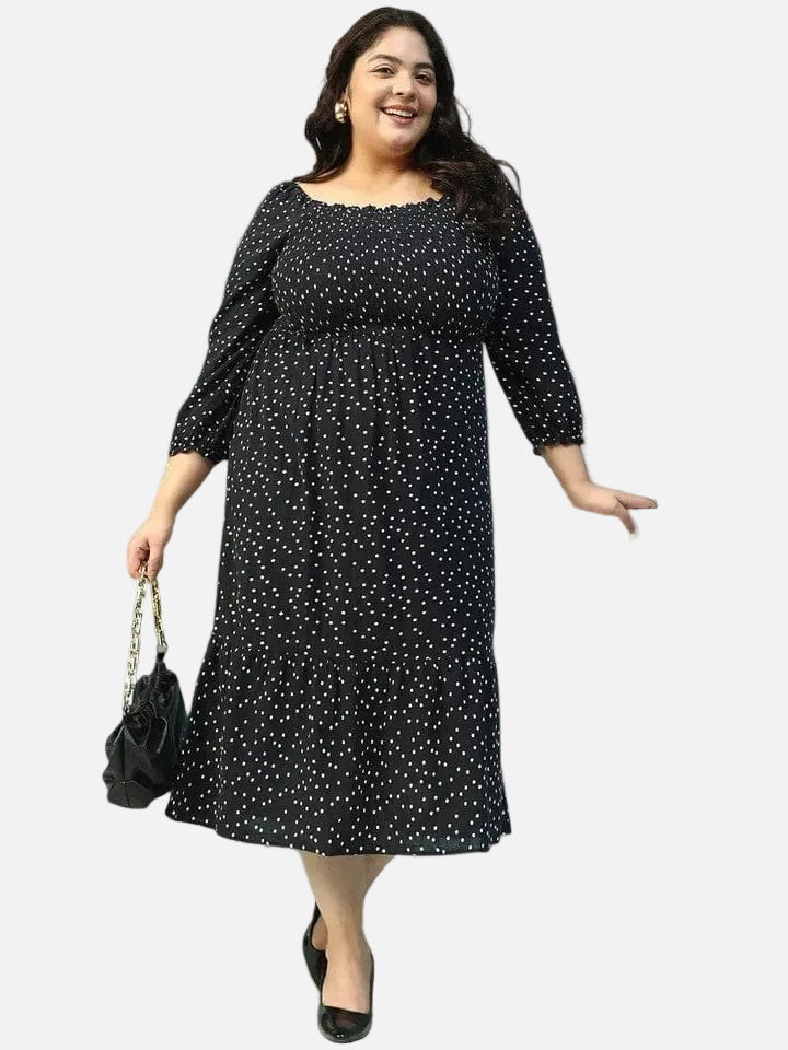 A woman wearing a black dress with white polka dots, smiling and holding a black purse.