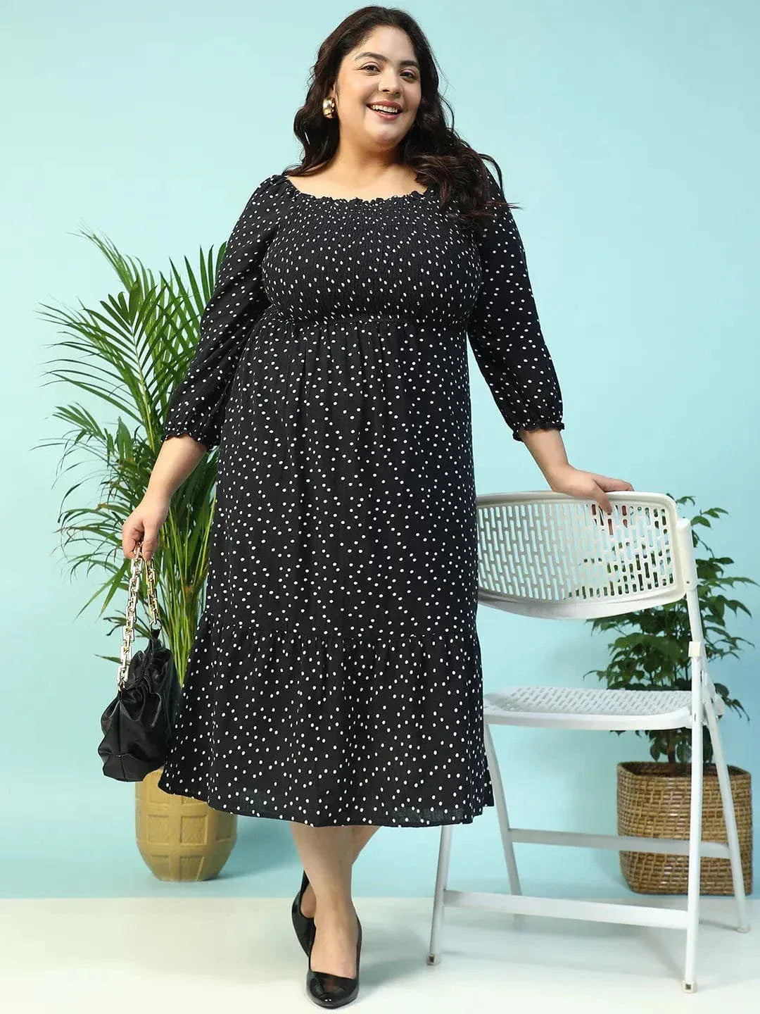 A woman wearing a black dress with white polka dots, smiling and holding a black purse.
