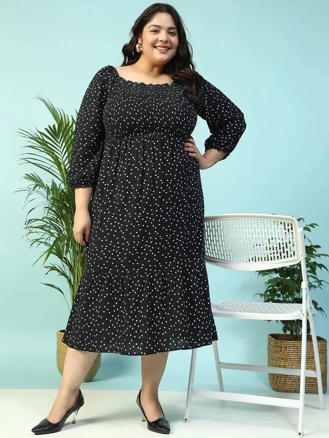 A woman wearing a black dress with white polka dots, smiling and holding a black purse.