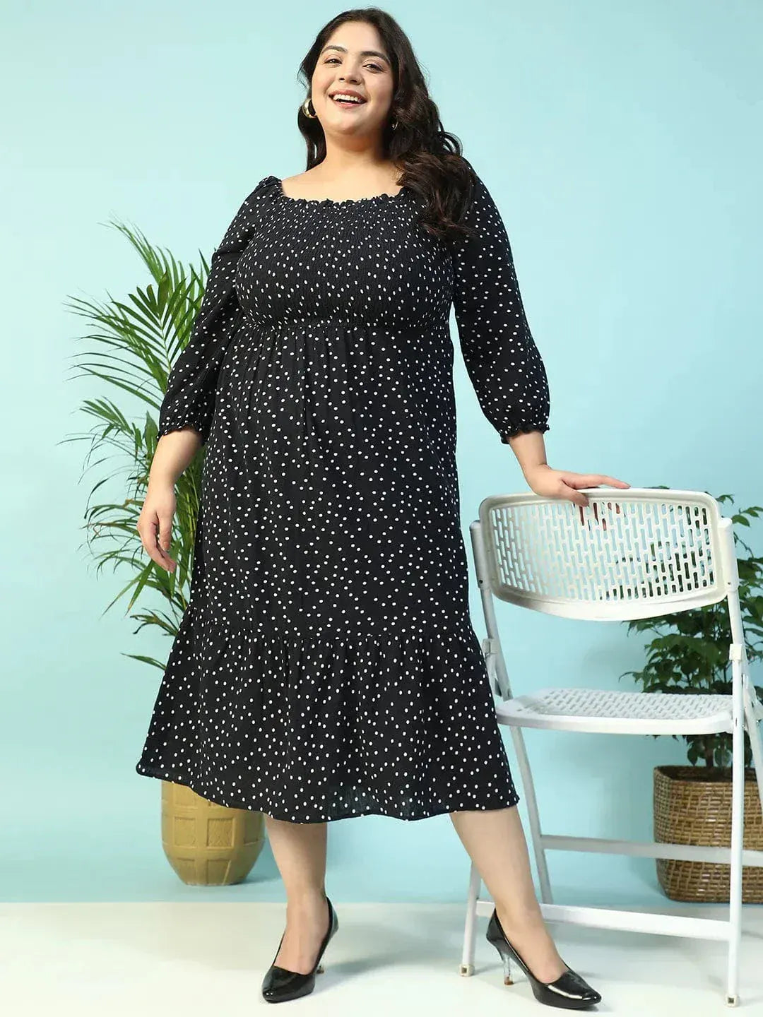 A woman wearing a black dress with white polka dots, smiling and holding a black purse.