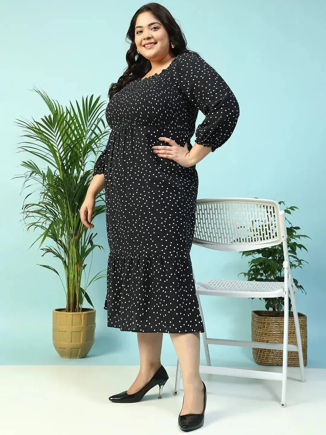 A woman wearing a black dress with white polka dots, smiling and holding a black purse.