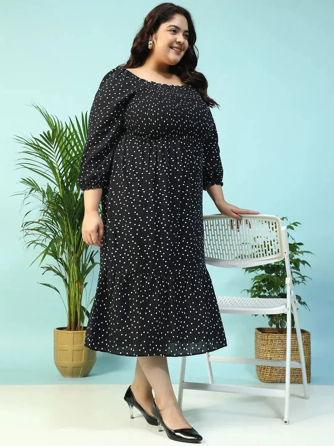 A woman wearing a black dress with white polka dots, smiling and holding a black purse.