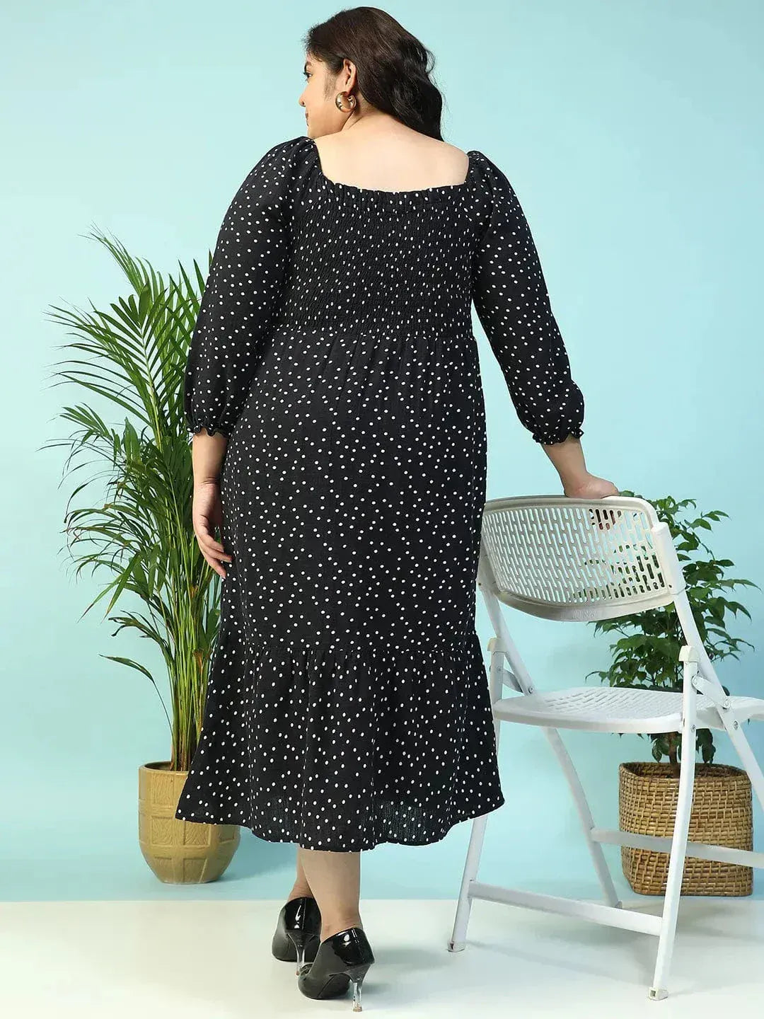 A woman wearing a black dress with white polka dots, smiling and holding a black purse.