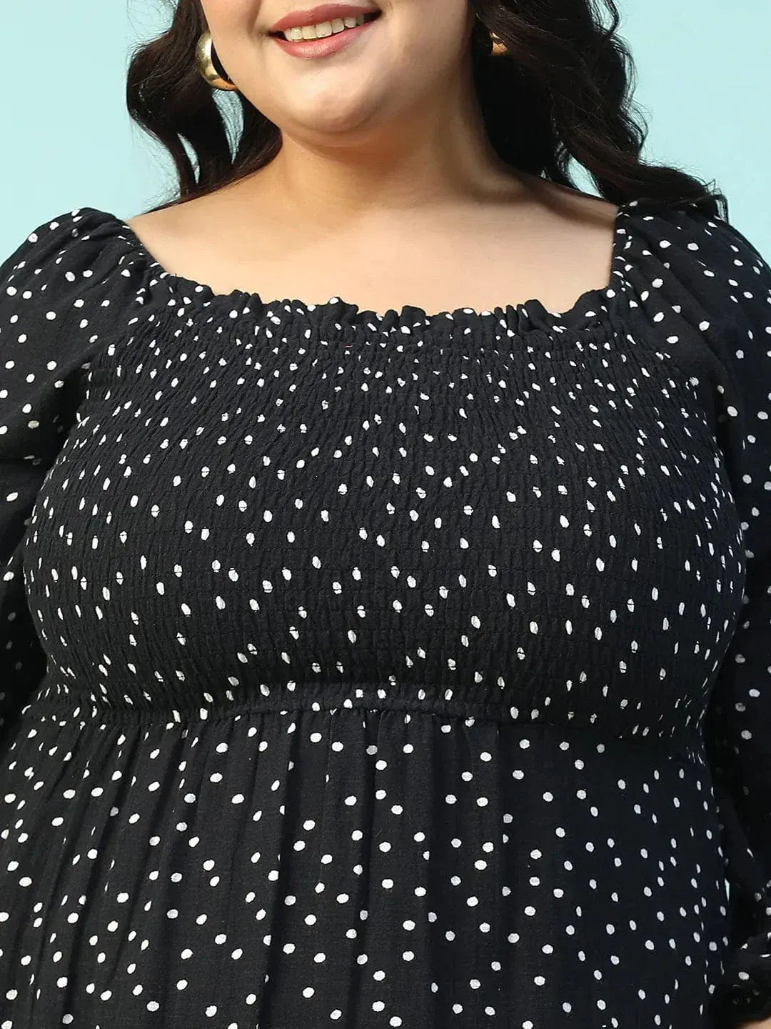 A woman wearing a black dress with white polka dots, smiling and holding a black purse.
