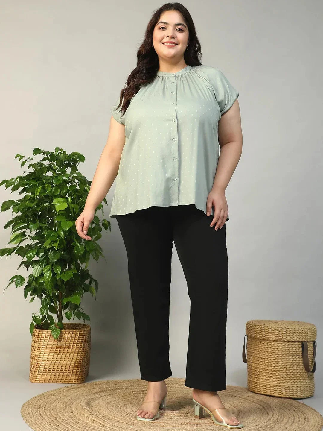 A woman with long brown hair is smiling and posing for the camera. She is wearing a light green blouse with a ruched collar and buttons.