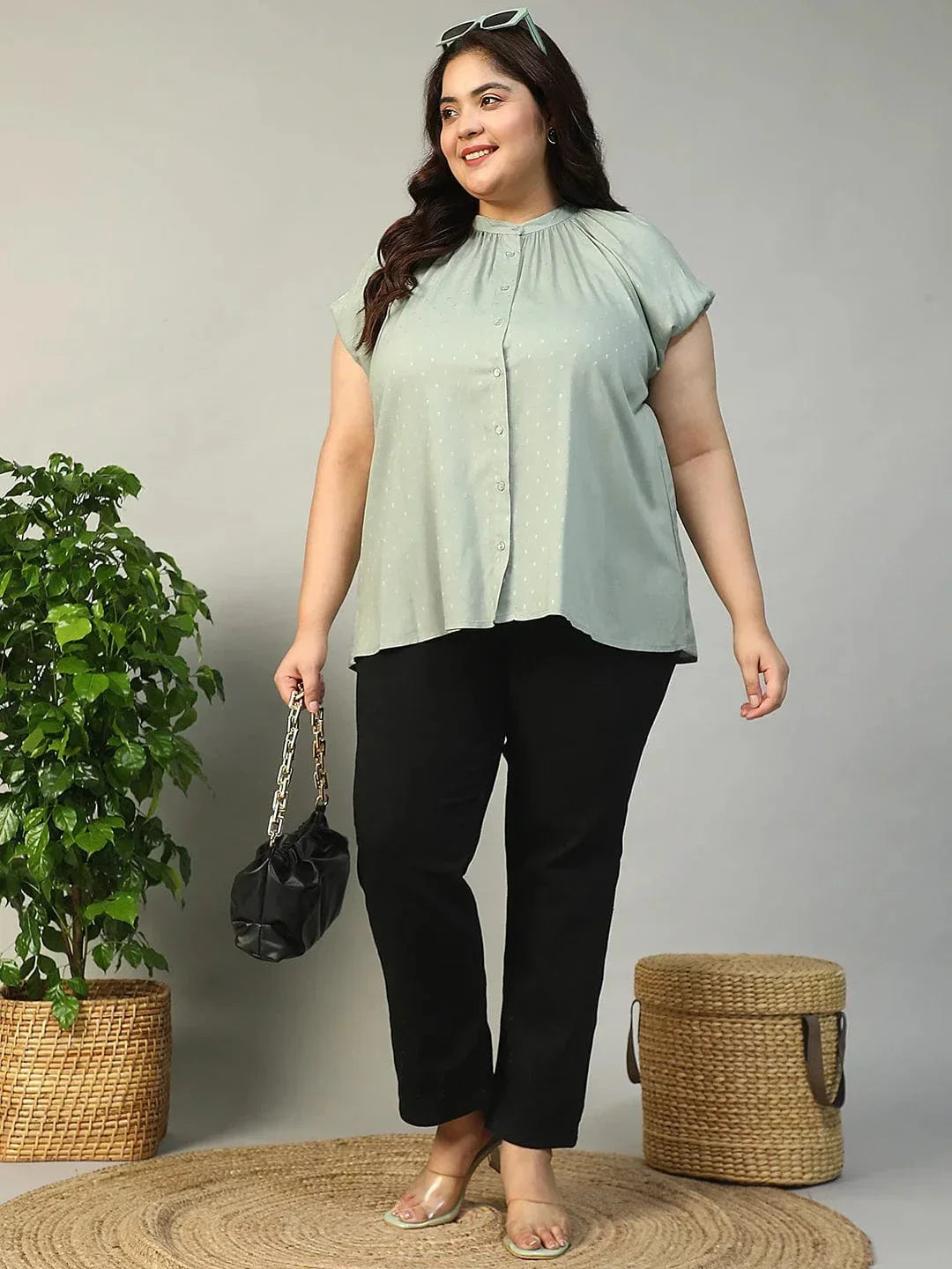 A woman with long brown hair is smiling and posing for the camera. She is wearing a light green blouse with a ruched collar and buttons.