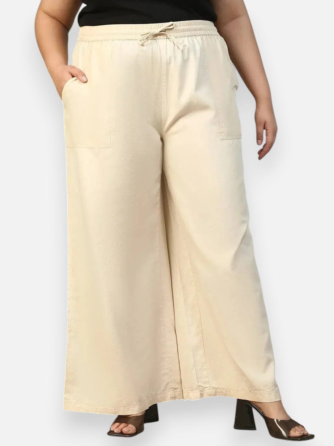 A person wearing a pair of wide-leg beige pants with a drawstring waist and high heels.