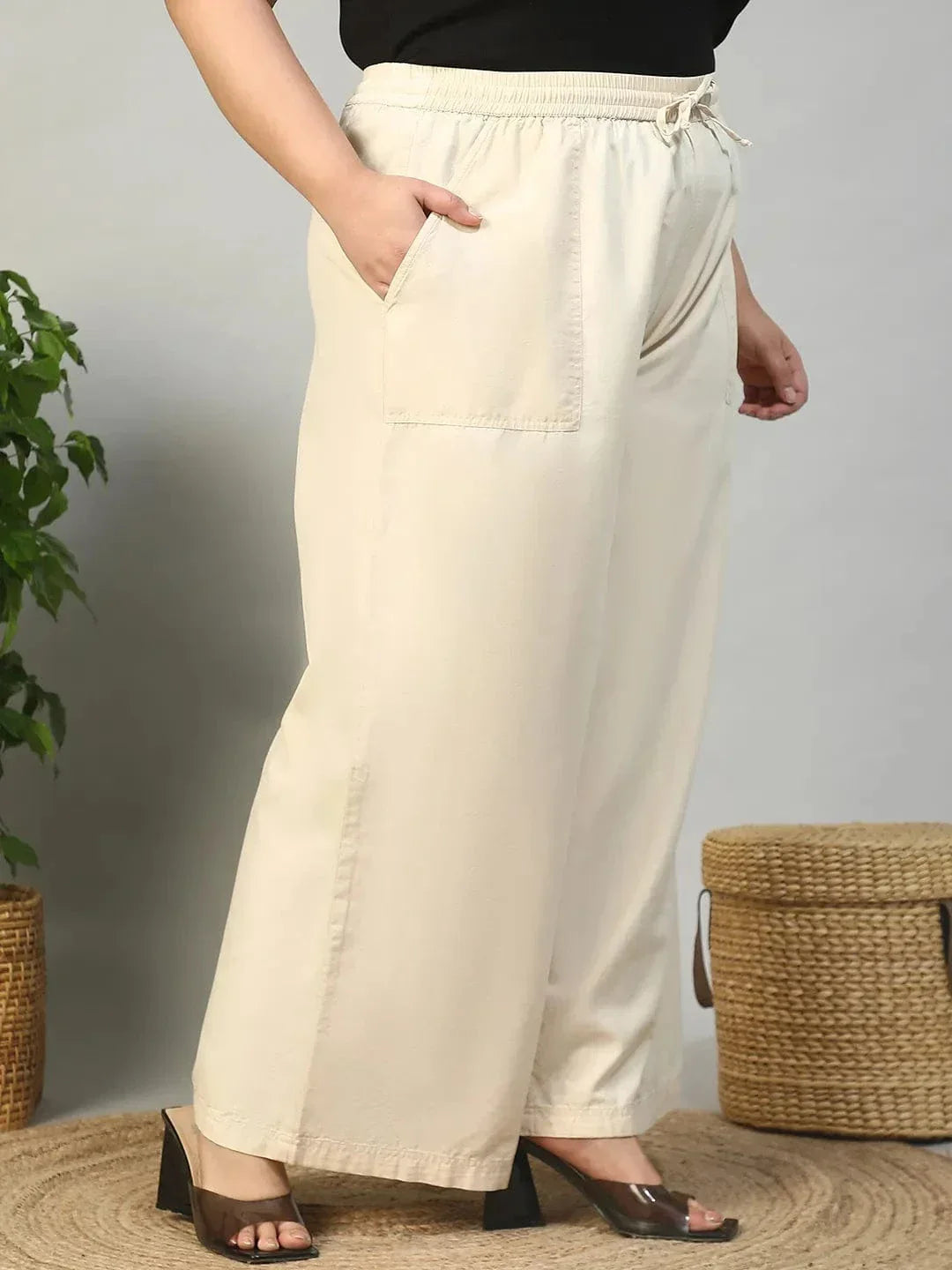 A person wearing a pair of wide-leg beige pants with a drawstring waist and high heels.
