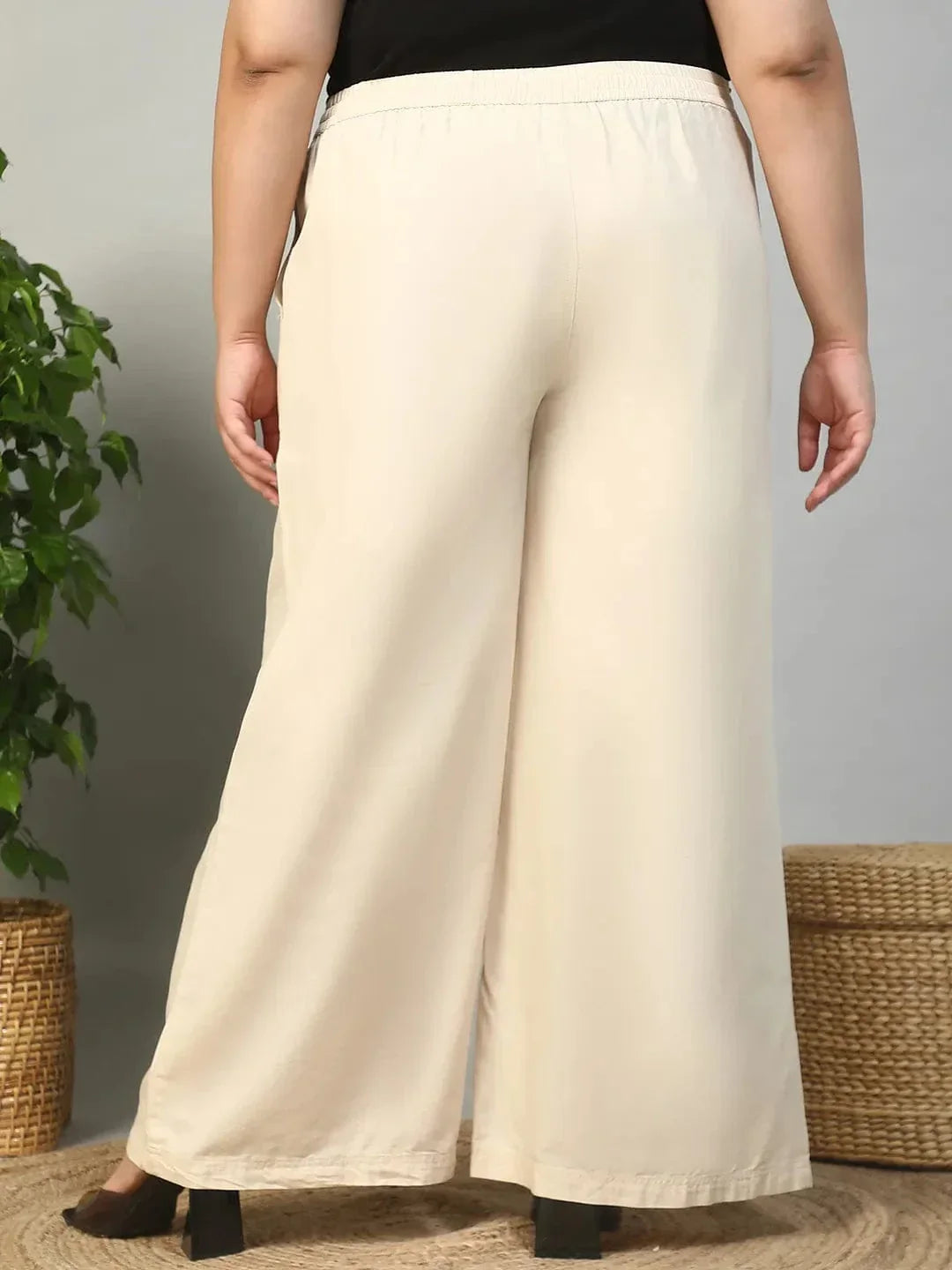 A person wearing a pair of wide-leg beige pants with a drawstring waist and high heels.