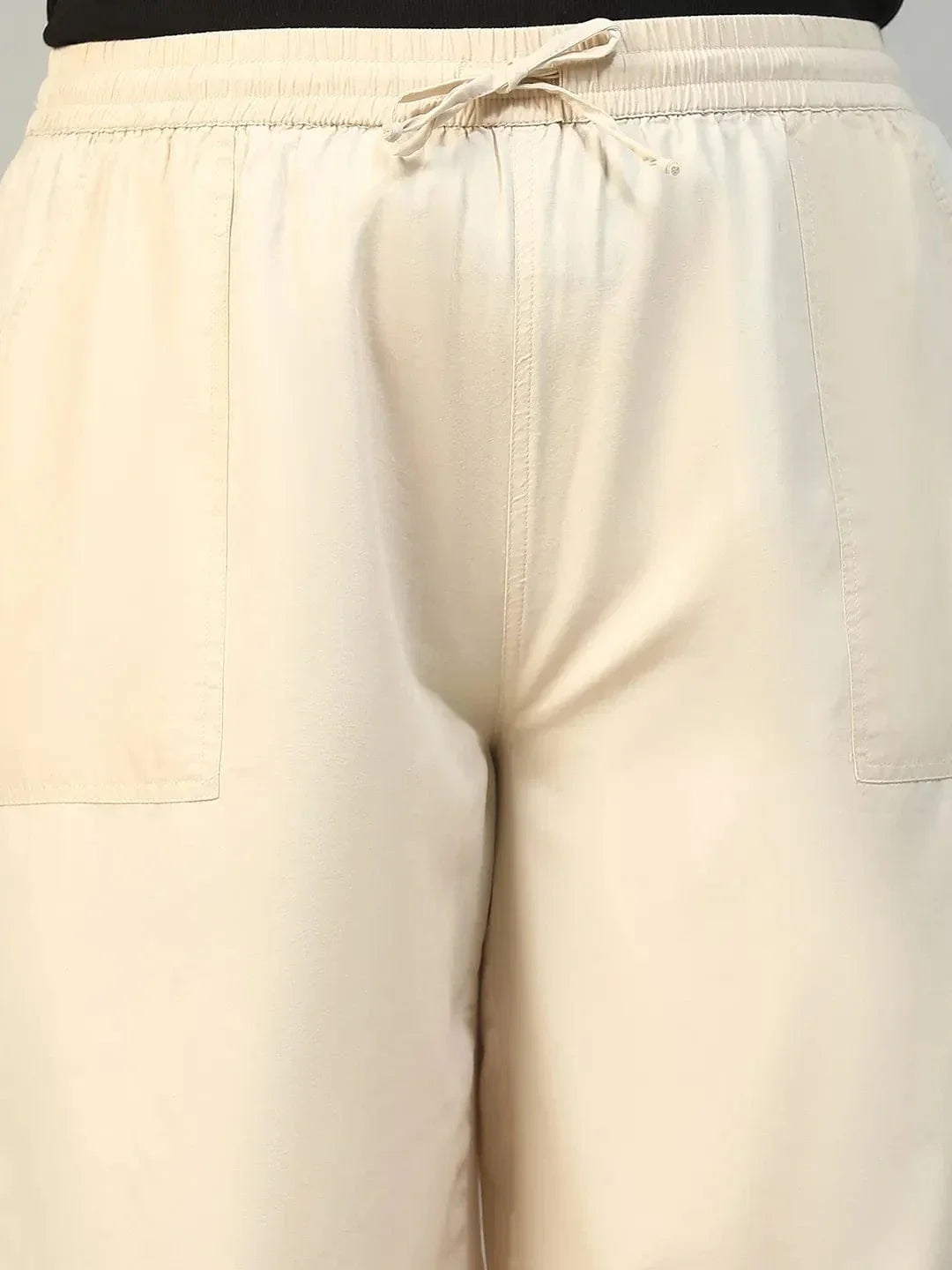 A person wearing a pair of wide-leg beige pants with a drawstring waist and high heels.