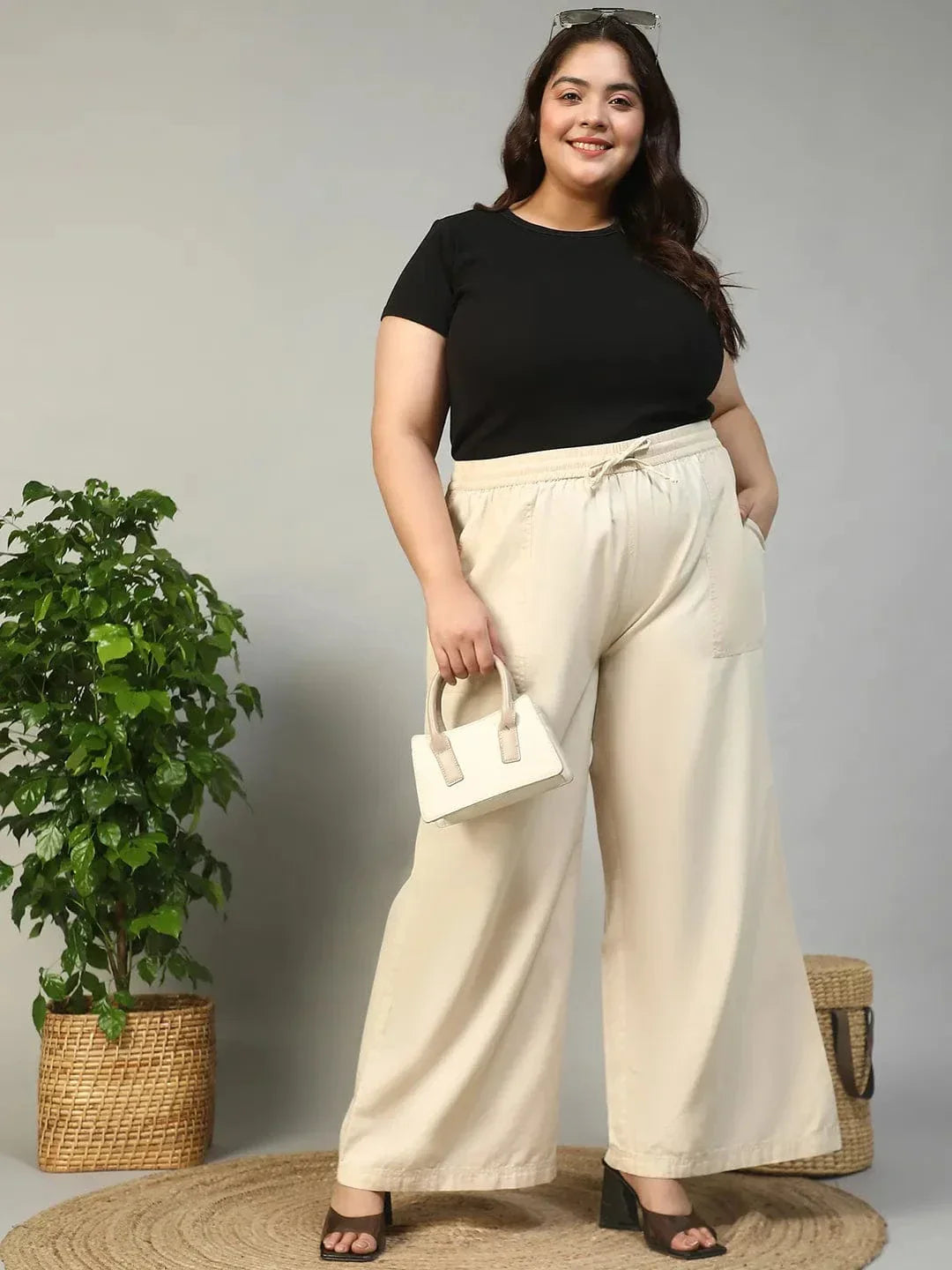 A person wearing a pair of wide-leg beige pants with a drawstring waist and high heels.