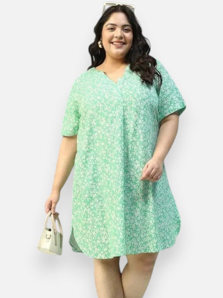 A smiling woman wearing a green floral print dress and holding a small white purse.