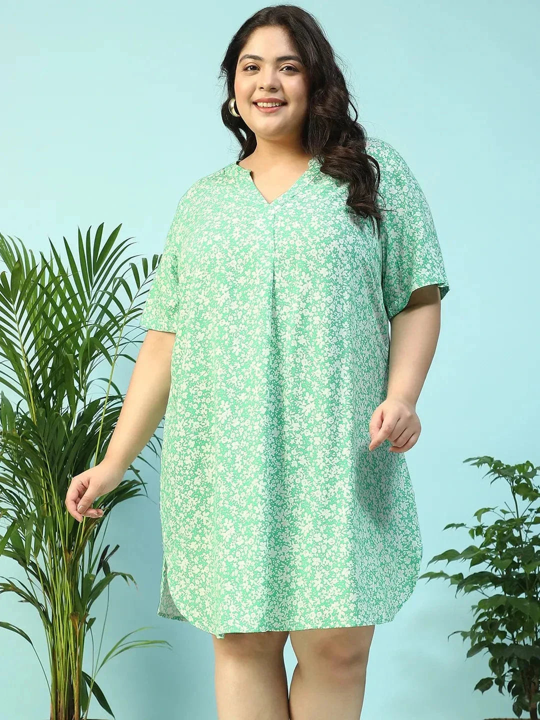 A smiling woman wearing a green floral print dress and holding a small white purse.