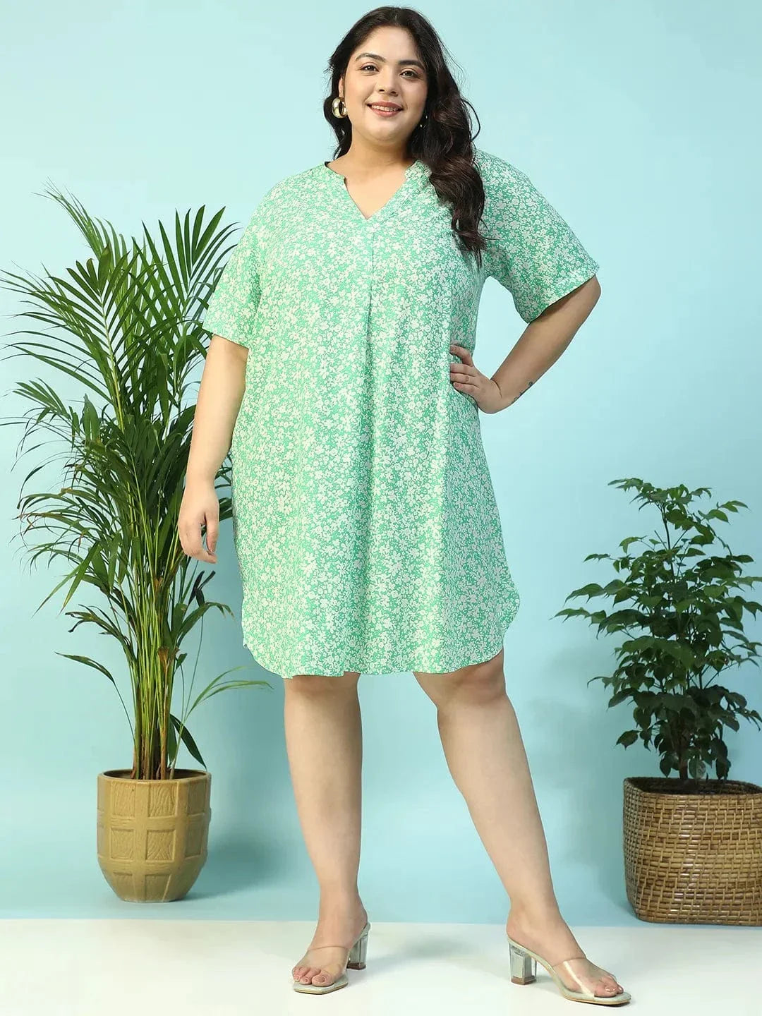 A smiling woman wearing a green floral print dress and holding a small white purse.