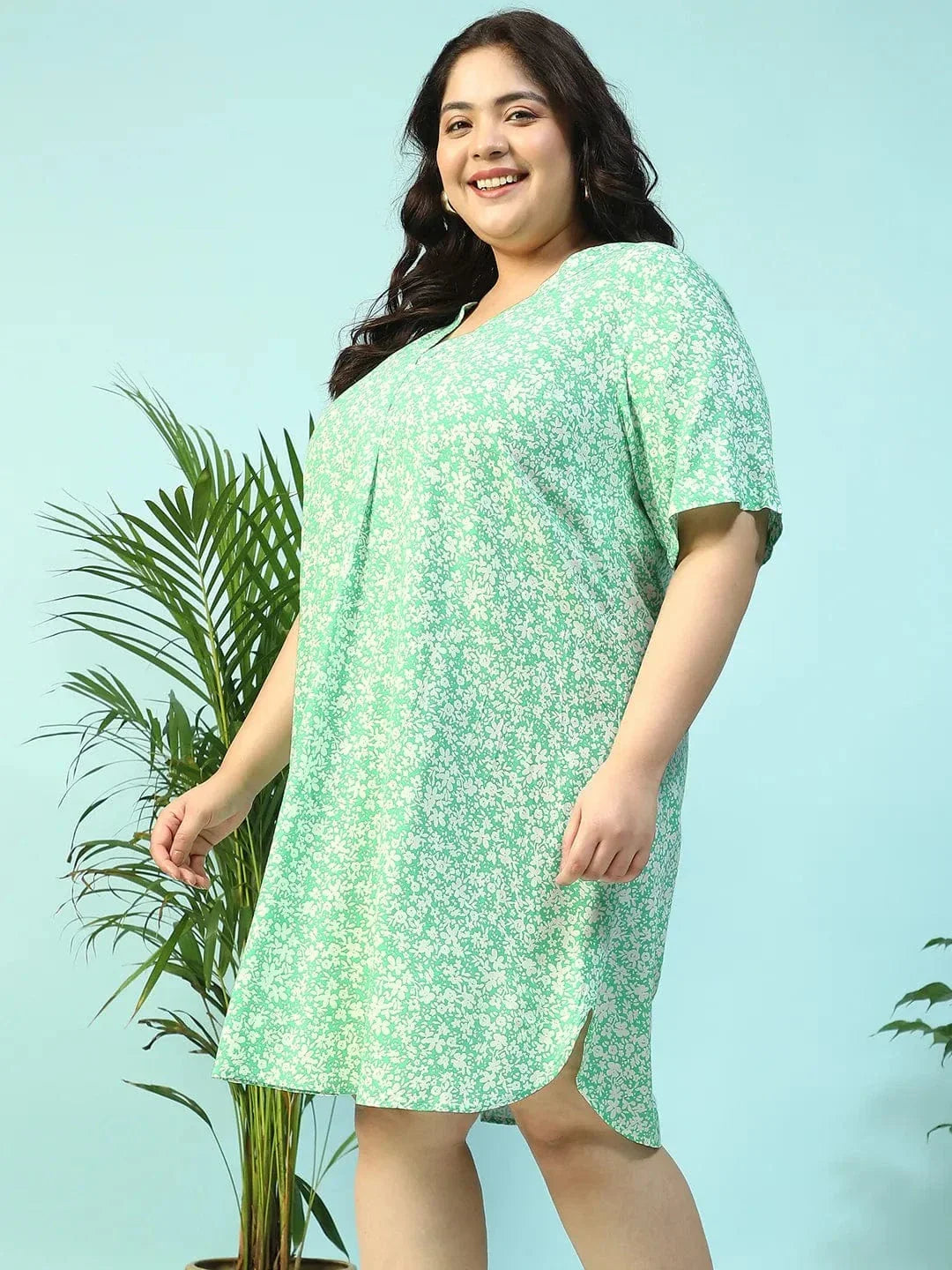 A smiling woman wearing a green floral print dress and holding a small white purse.