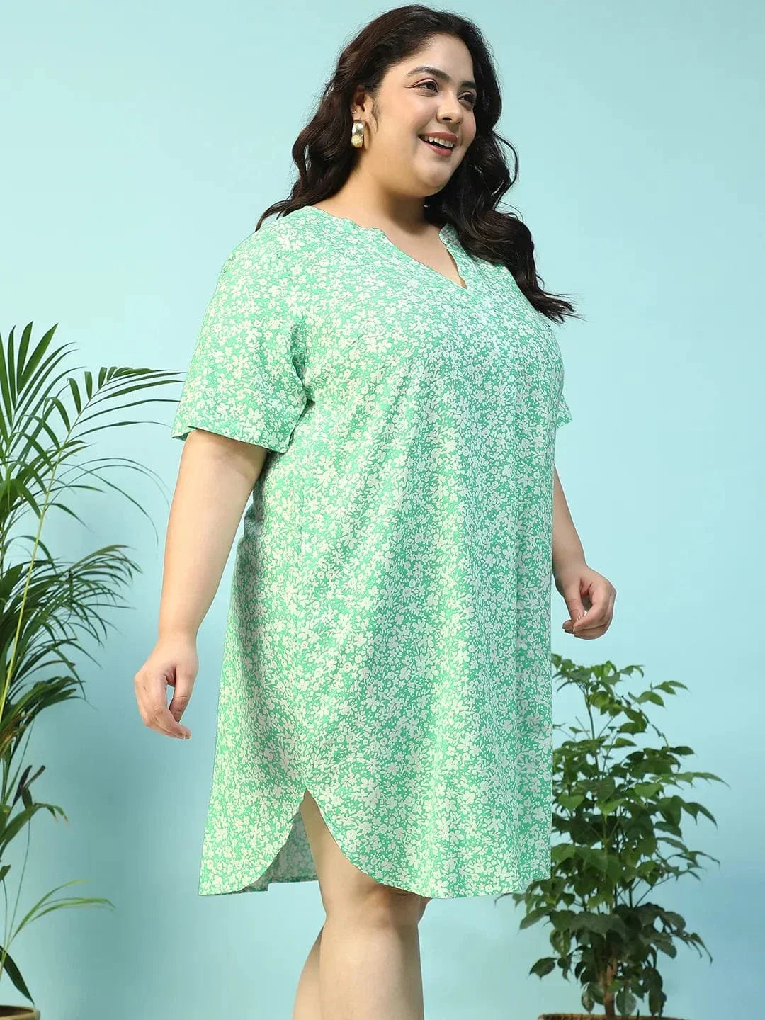 A smiling woman wearing a green floral print dress and holding a small white purse.