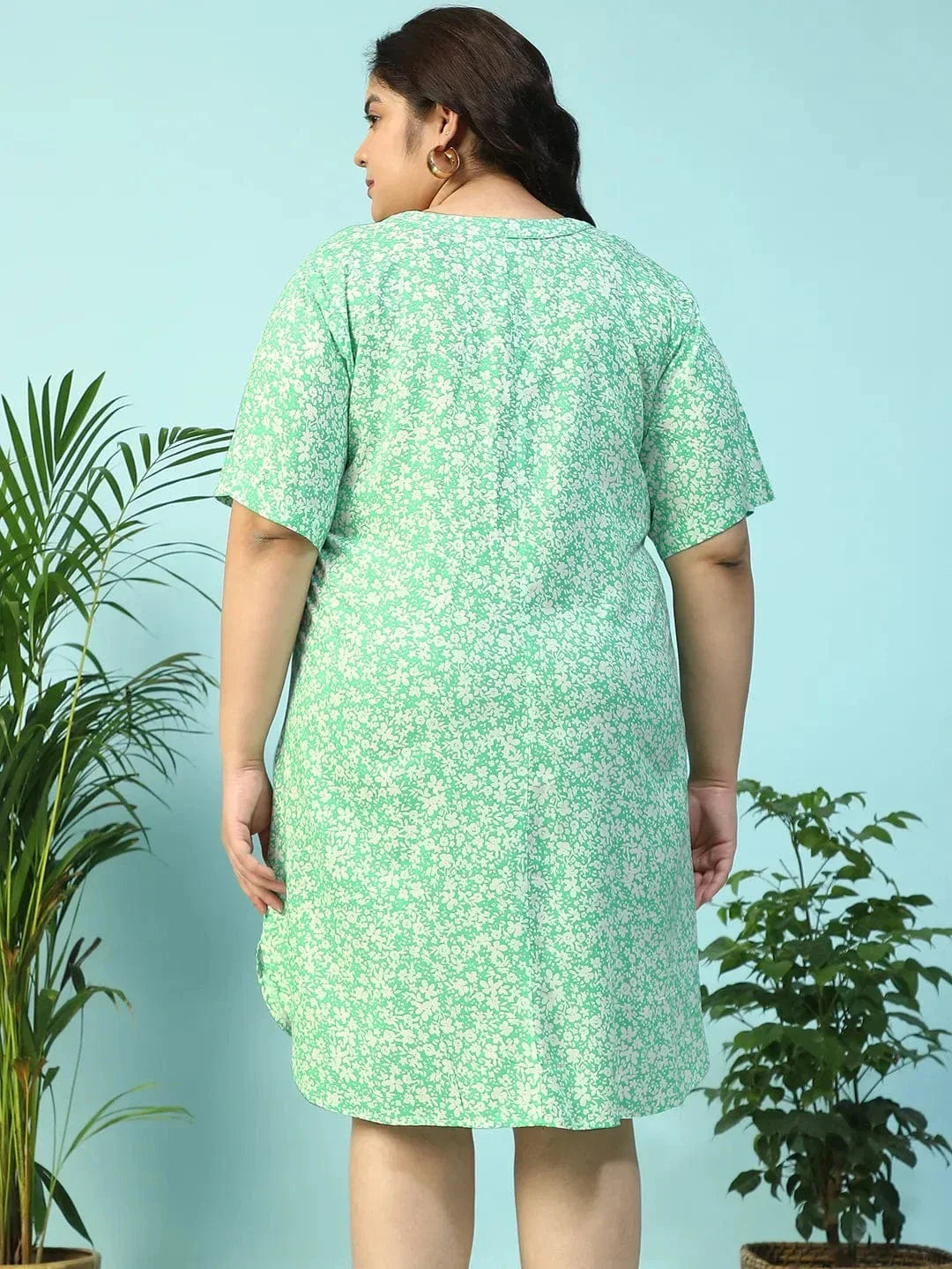 A smiling woman wearing a green floral print dress and holding a small white purse.