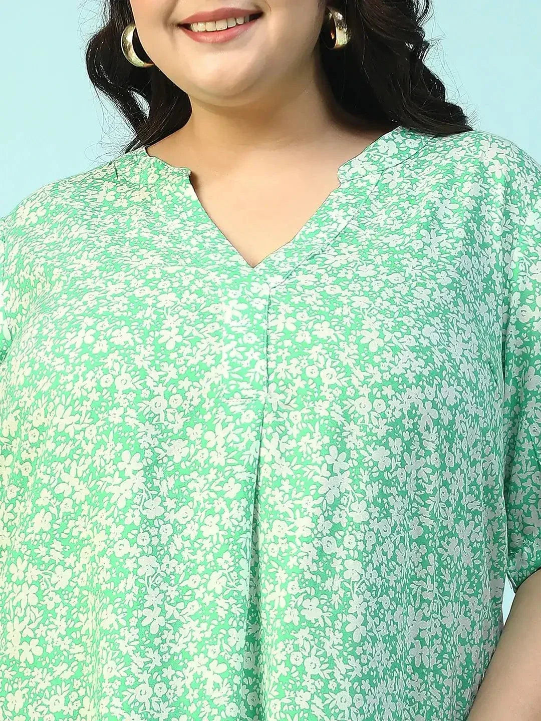 A smiling woman wearing a green floral print dress and holding a small white purse.