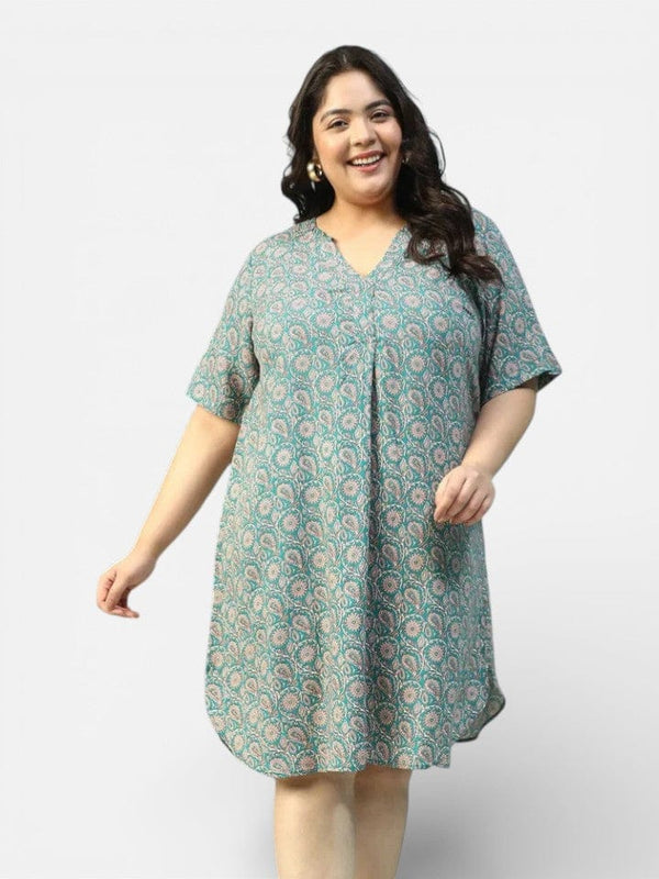 A smiling woman wearing a green and white patterned dress stands against a white background.