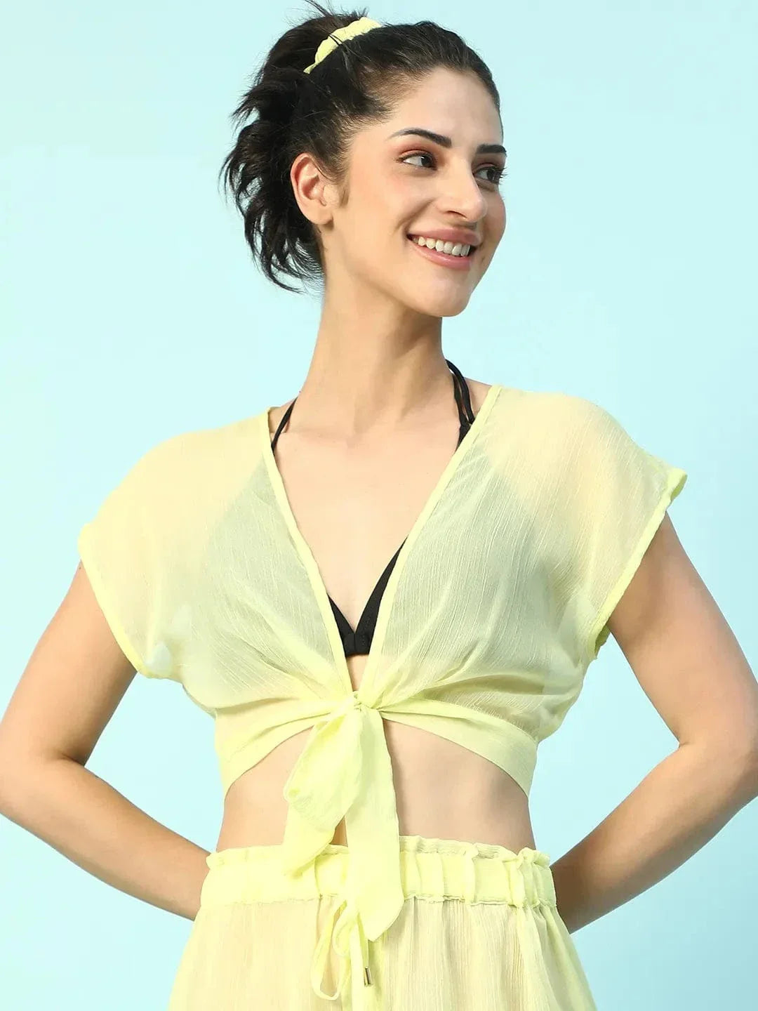 A woman wearing a yellow crop top and skirt is smiling and posing confidently.