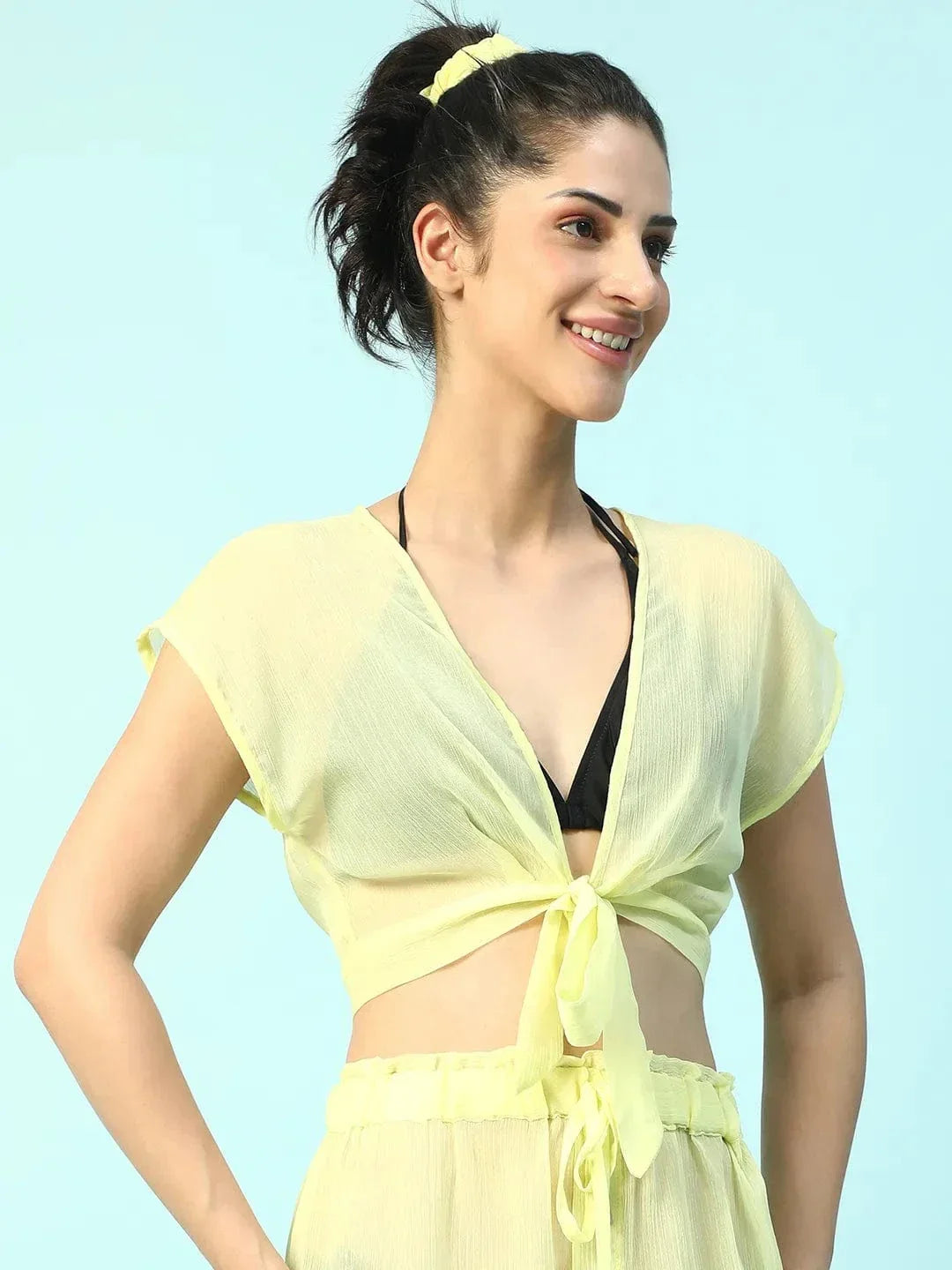 A woman wearing a yellow crop top and skirt is smiling and posing confidently.