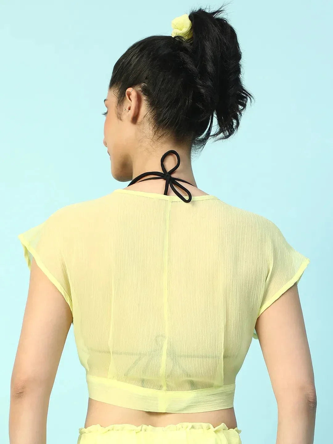 A woman wearing a yellow crop top and skirt is smiling and posing confidently.