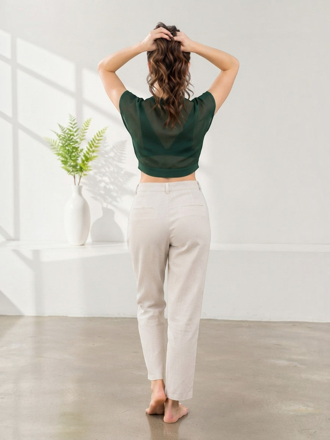 Woman in green sheer crop top and beige high-waist pants, back view, modern minimalist style