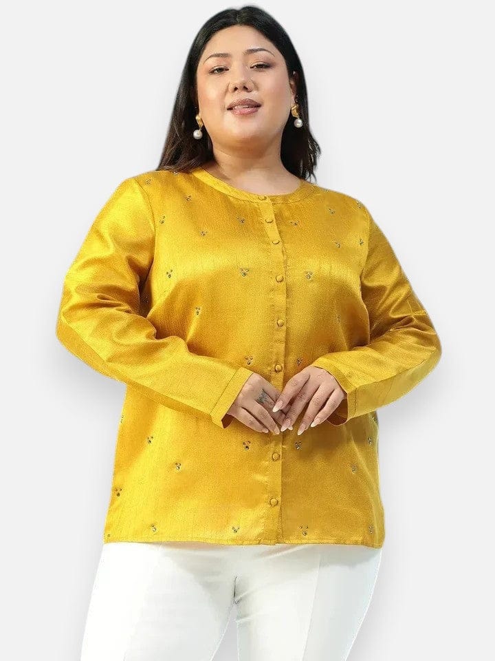 A woman wearing a yellow blouse with small embroidered designs, posing for a photograph.