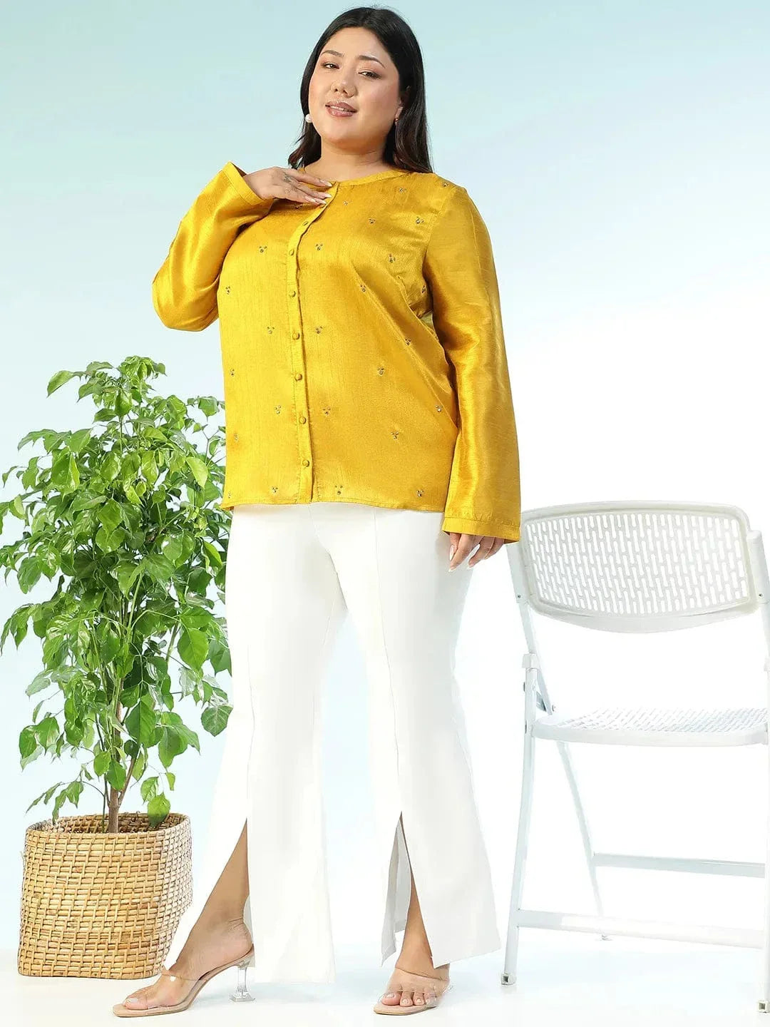 A woman wearing a yellow blouse with small embroidered designs, posing for a photograph.