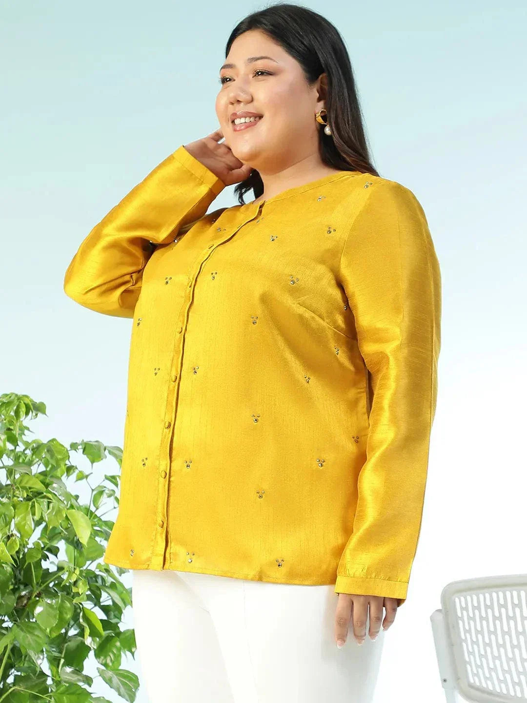 A woman wearing a yellow blouse with small embroidered designs, posing for a photograph.