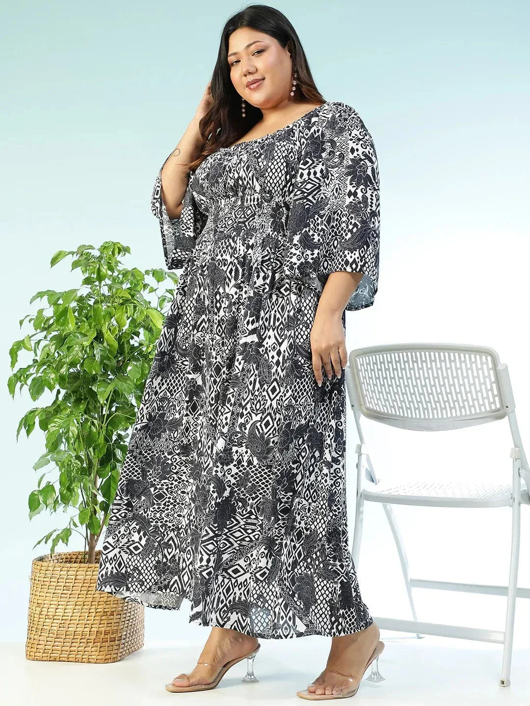 A woman wearing a long, black and white patterned dress with a high neckline and long sleeves, posing with a white purse.