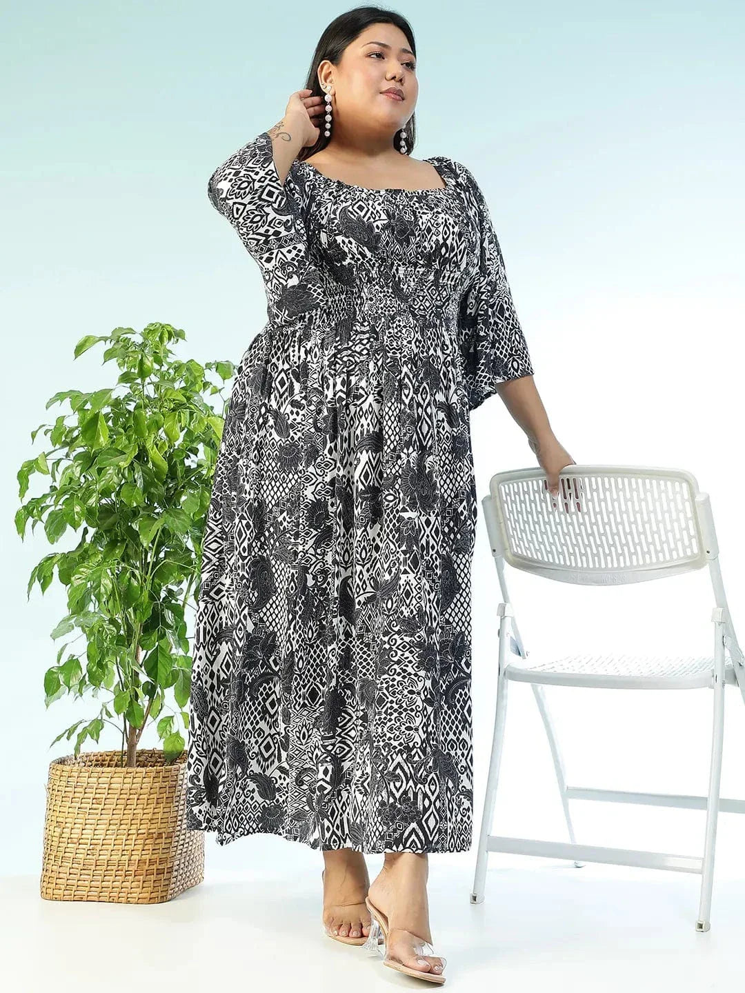 A woman wearing a long, black and white patterned dress with a high neckline and long sleeves, posing with a white purse.
