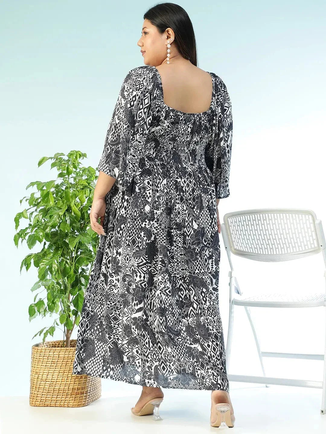 A woman wearing a long, black and white patterned dress with a high neckline and long sleeves, posing with a white purse.