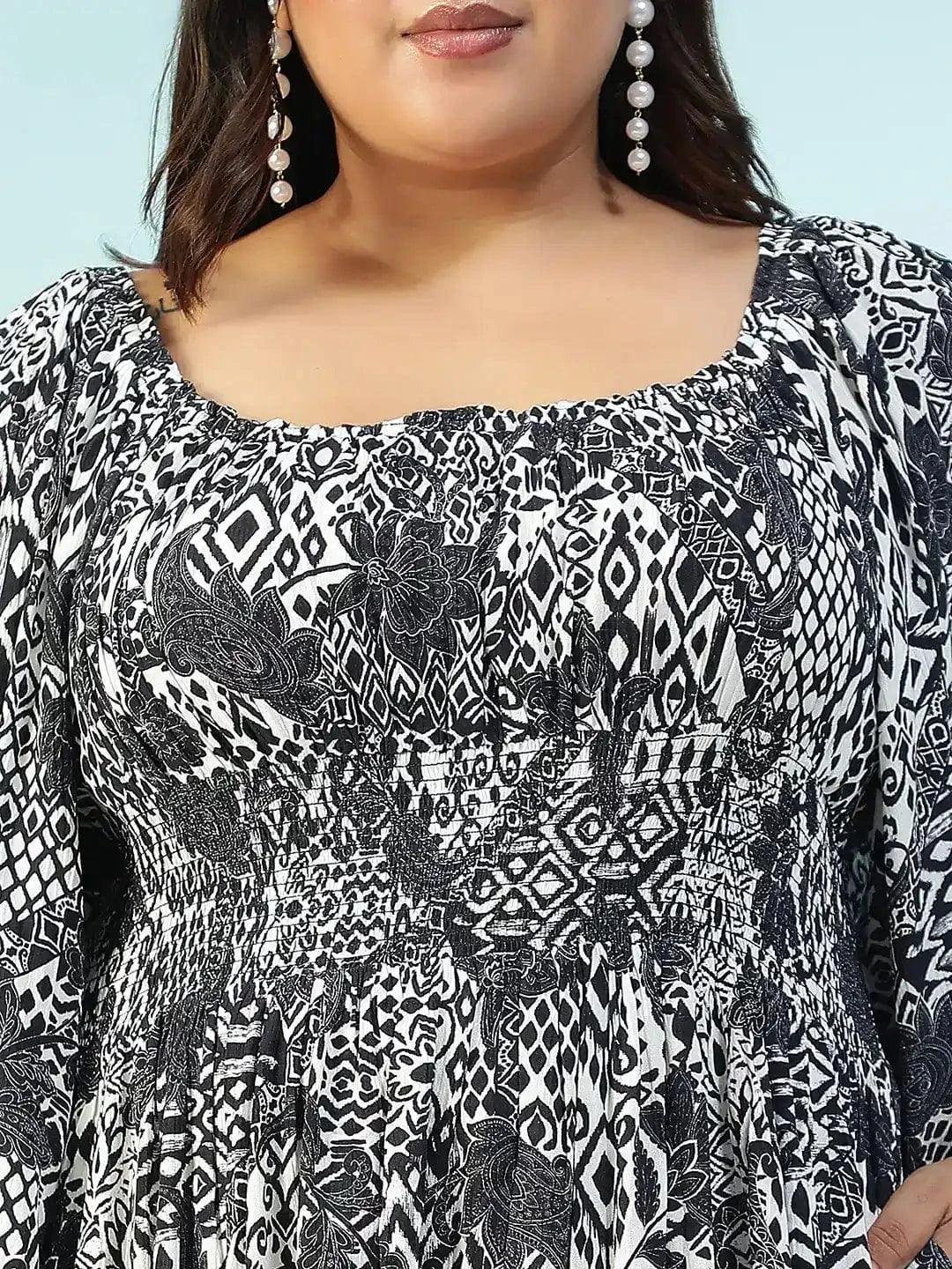 A woman wearing a long, black and white patterned dress with a high neckline and long sleeves, posing with a white purse.