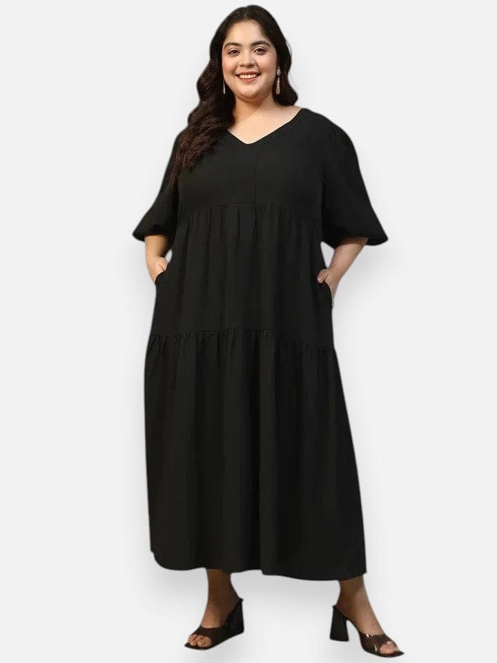 A woman wearing a long black dress with a v-neck and flared sleeves, smiling at the camera.