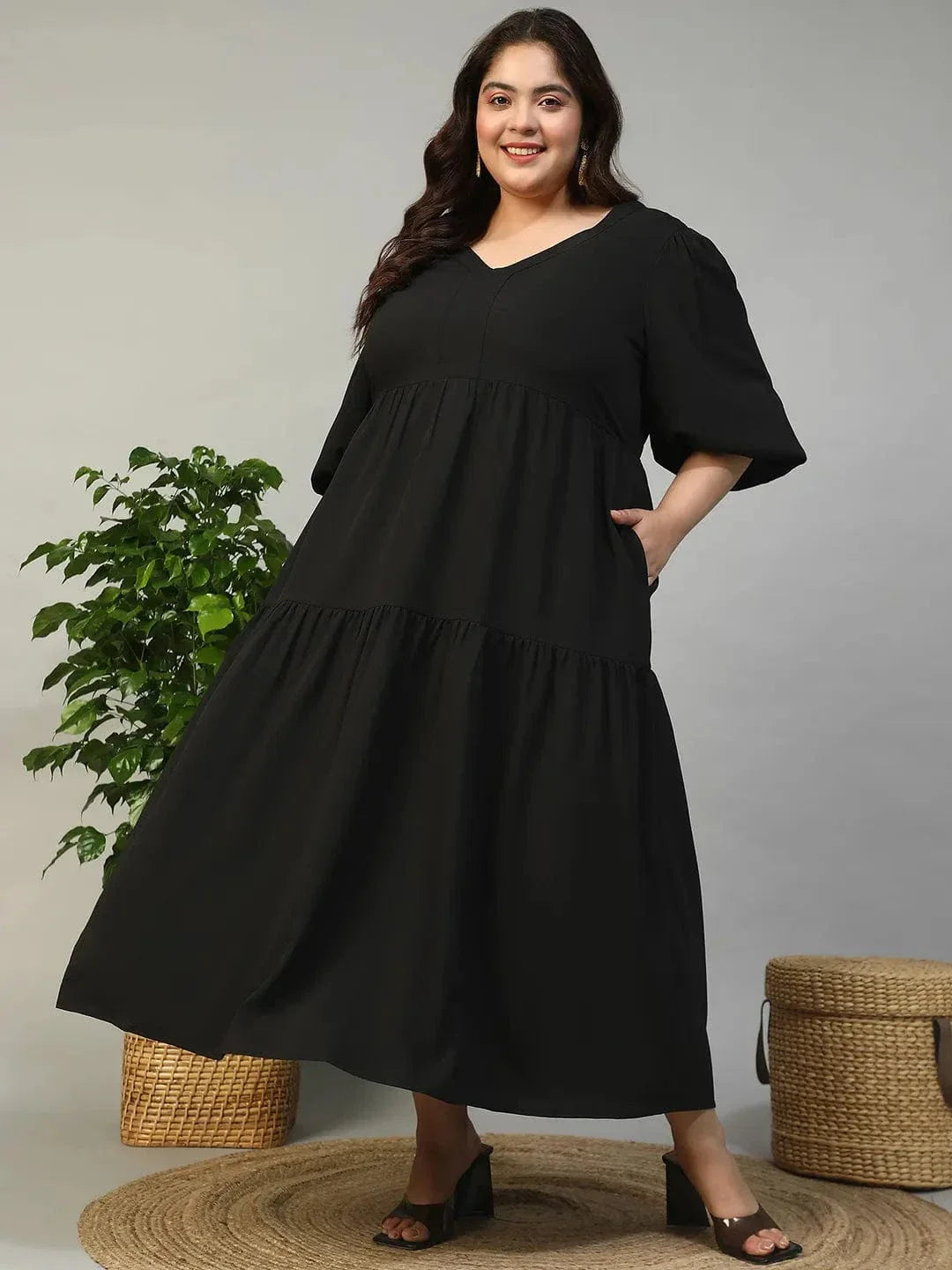 A woman wearing a long black dress with a v-neck and flared sleeves, smiling at the camera.