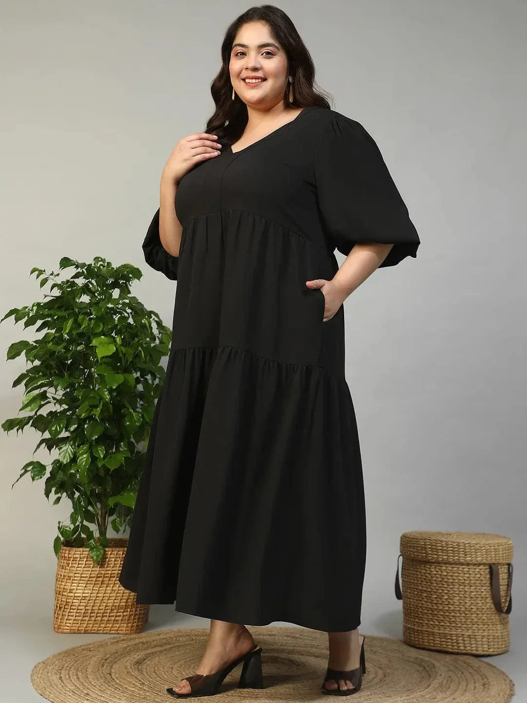A woman wearing a long black dress with a v-neck and flared sleeves, smiling at the camera.