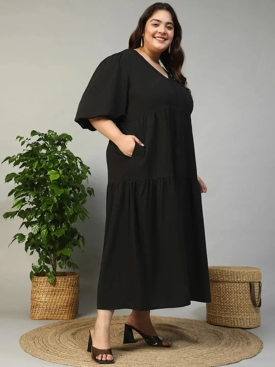 A woman wearing a long black dress with a v-neck and flared sleeves, smiling at the camera.