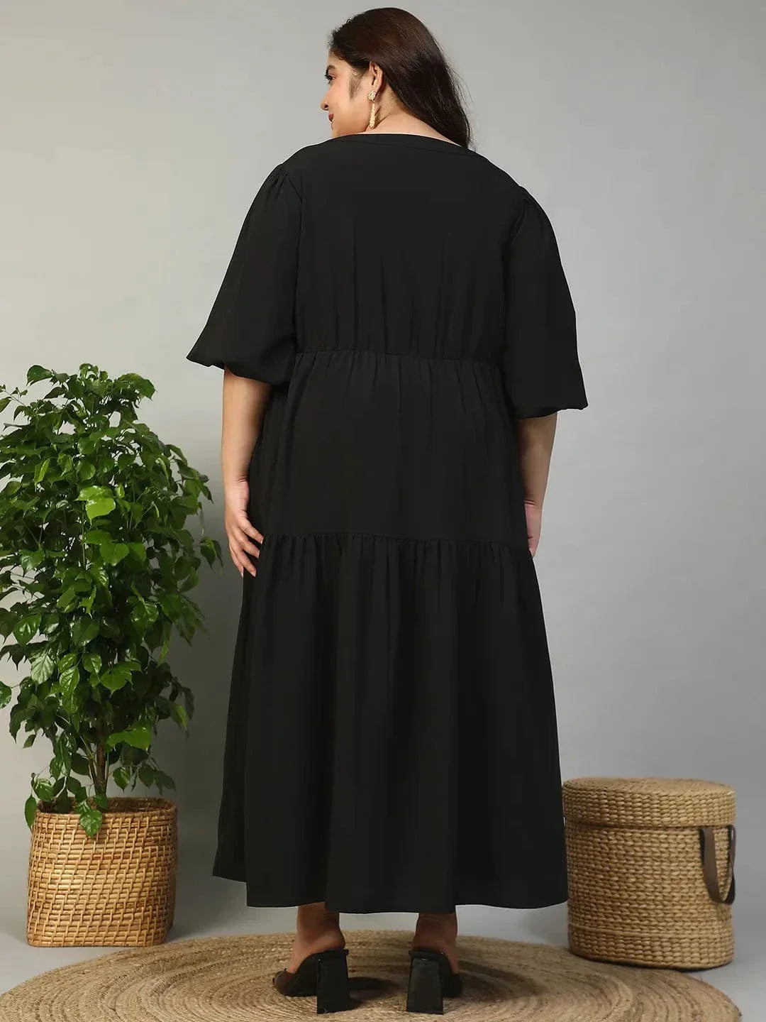 A woman wearing a long black dress with a v-neck and flared sleeves, smiling at the camera.