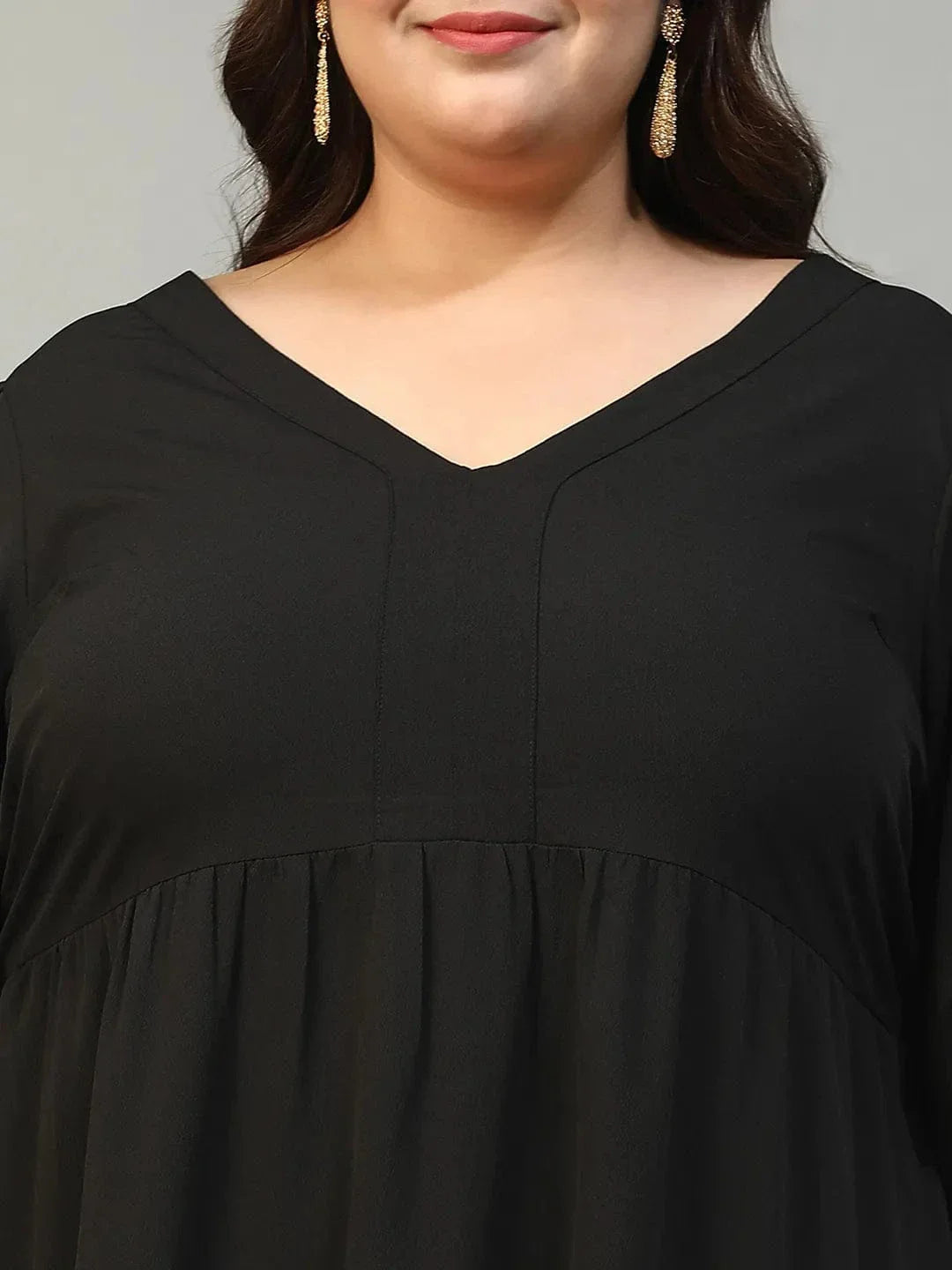 A woman wearing a long black dress with a v-neck and flared sleeves, smiling at the camera.