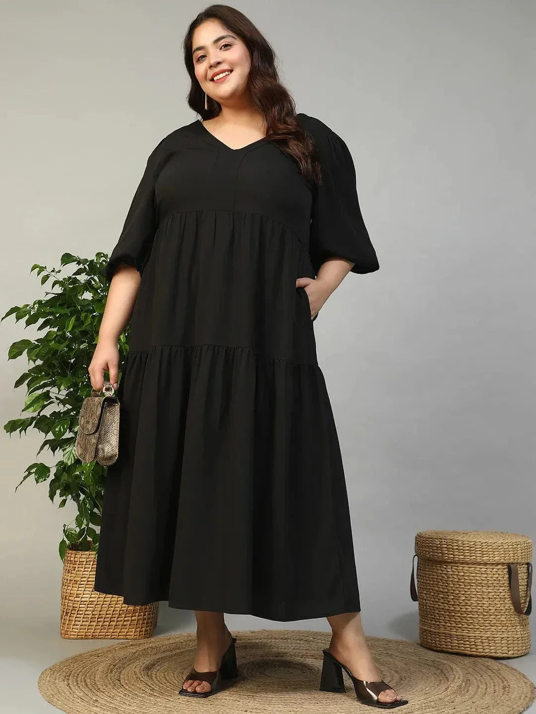 A woman wearing a long black dress with a v-neck and flared sleeves, smiling at the camera.