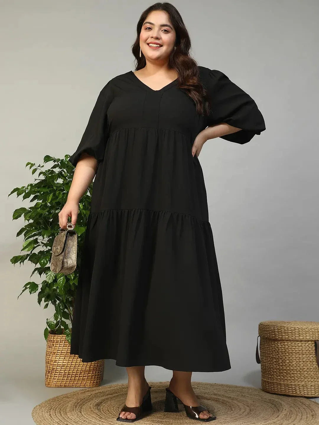 A woman wearing a long black dress with a v-neck and flared sleeves, smiling at the camera.