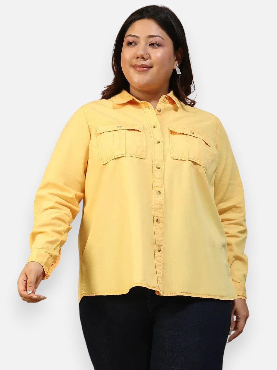 A woman wearing a yellow button-up shirt and black pants is smiling and looking to the side.