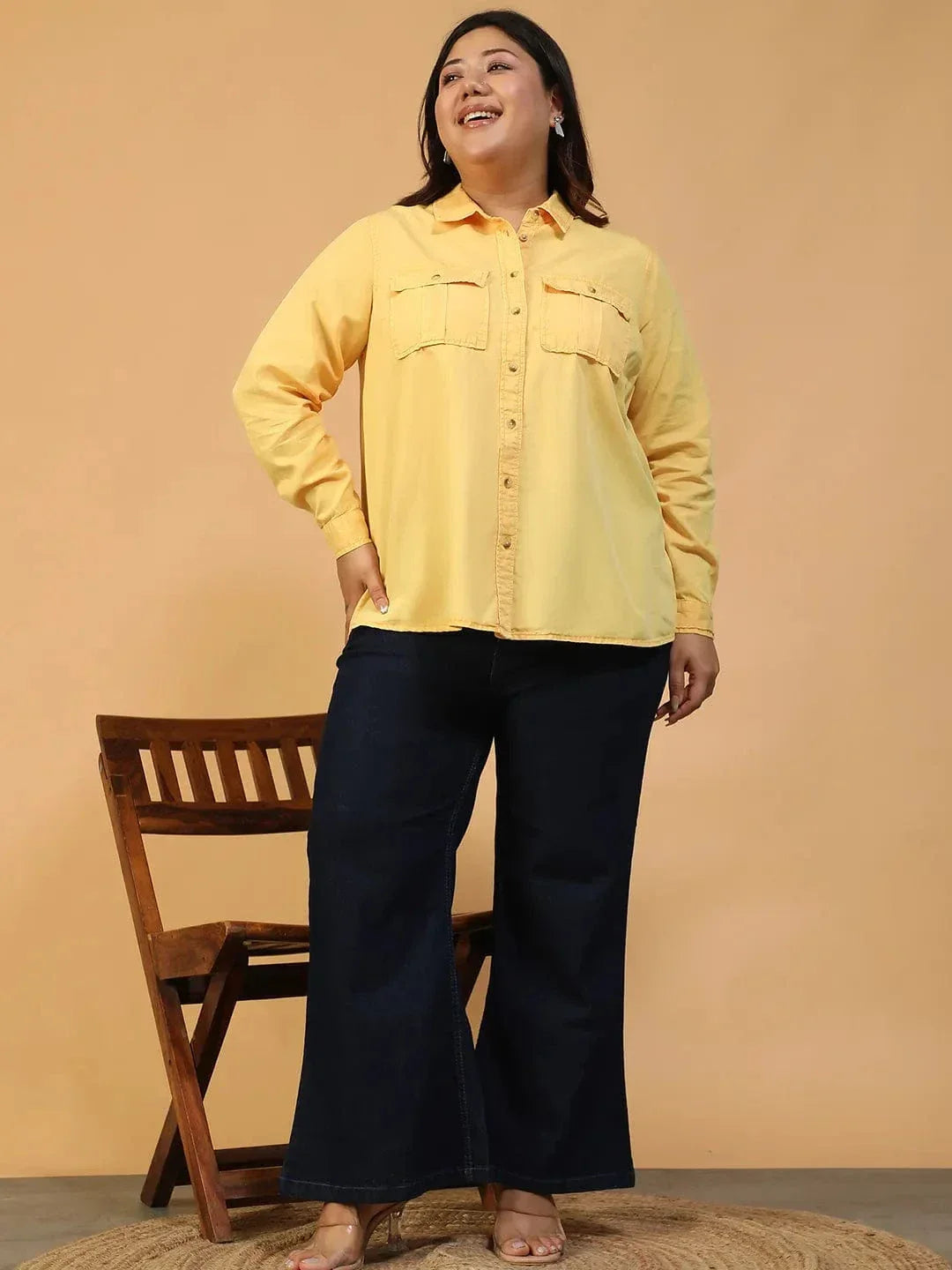 A woman wearing a yellow button-up shirt and black pants is smiling and looking to the side.